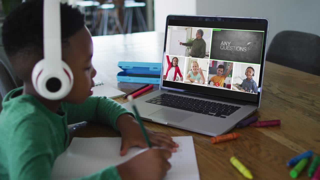 Schoolboy using laptop for online lesson at home, with diverse teacher and class on screen