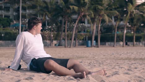 guy-in-white-shirt-rests-on-ocean-beach-against-palm-trees