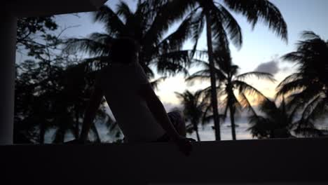 Man-looking-into-sunset-with-palm-trees-and-ocean-view