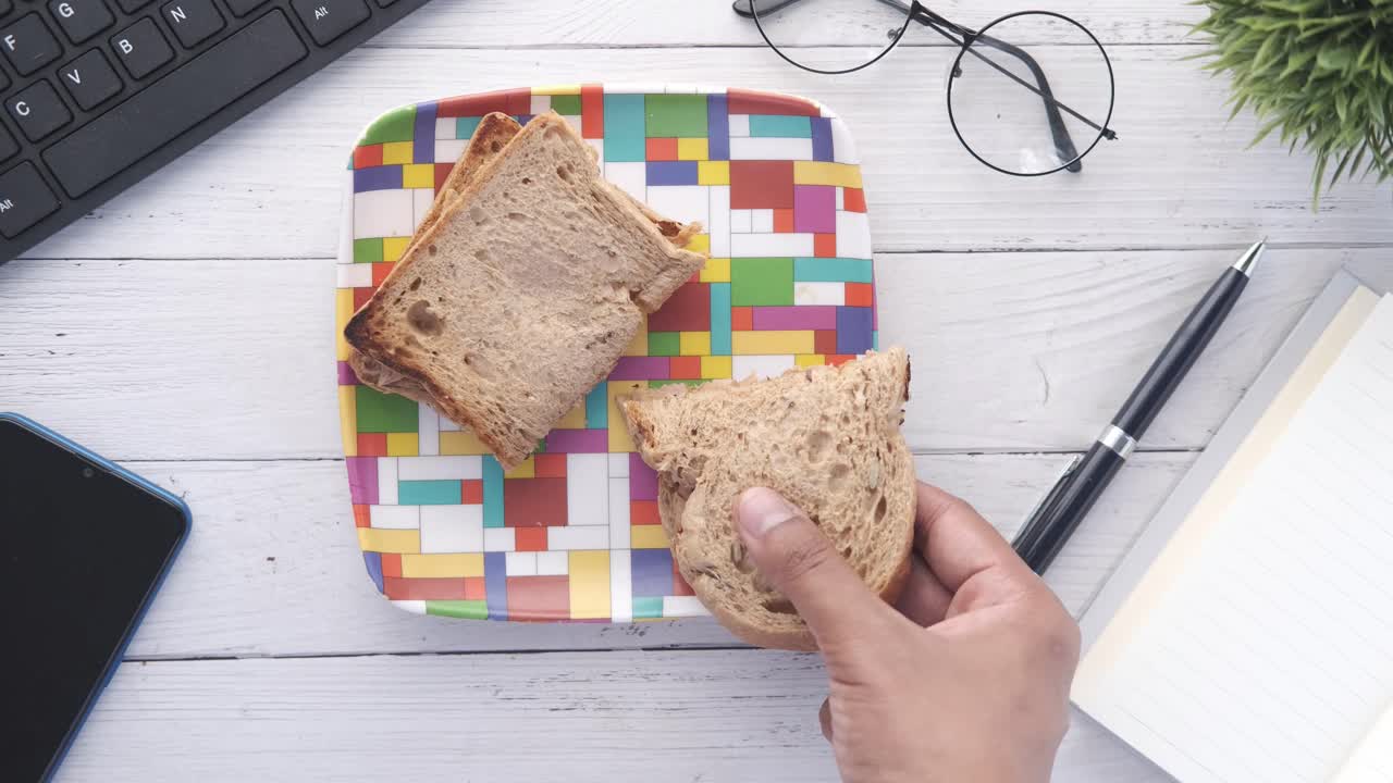 책상 위에 있는 접시 위에 샌드위치를 들고 있는 손