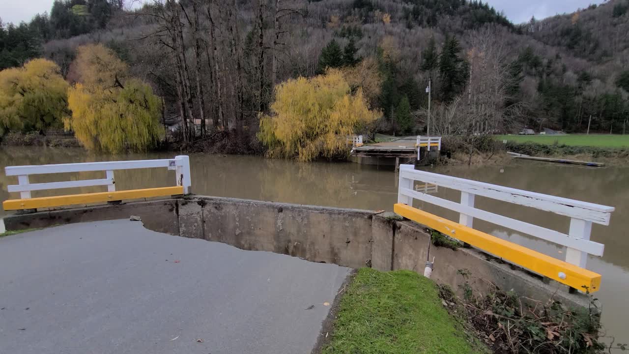 dolly adelante hacia el puente derrumbado sobre el río en abbotsford, bc, canadá con inclinación hacia abajo revelando asfalto hundido