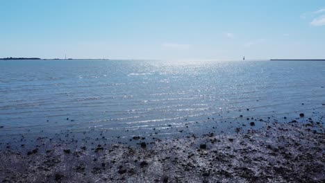 Die-Grenzenlosen-Gewässer-Des-Hafens-Von-Felixstowe-Erstrahlen-In-Den-Lichtstrahlen,-Während-Die-Verschwommene-Silhouette-Eines-Bootes-Am-Horizont-Funkelt