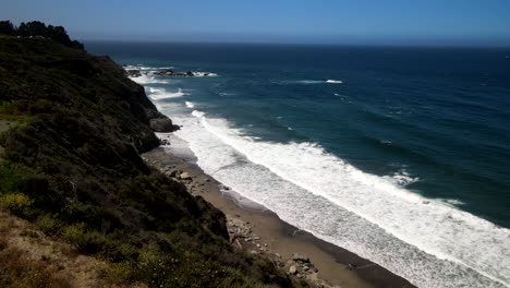 aerial drone captures cinematic shots of the big sur coastline, showcasing waves crashing onto the shore and the vast blue ocean