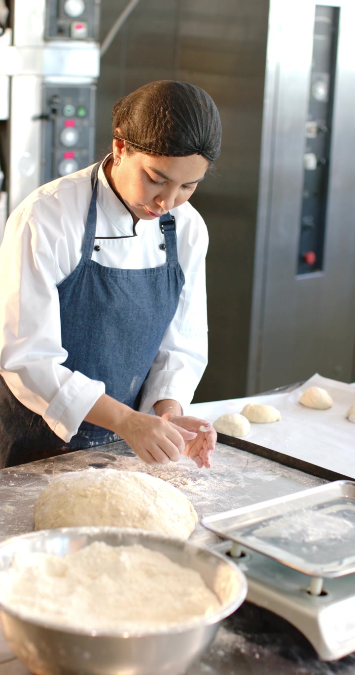 Diversas compañeras de trabajo espolvoreando harina, amasando y dando forma a una gran cantidad de masa en una mesa de preparación para hornear.