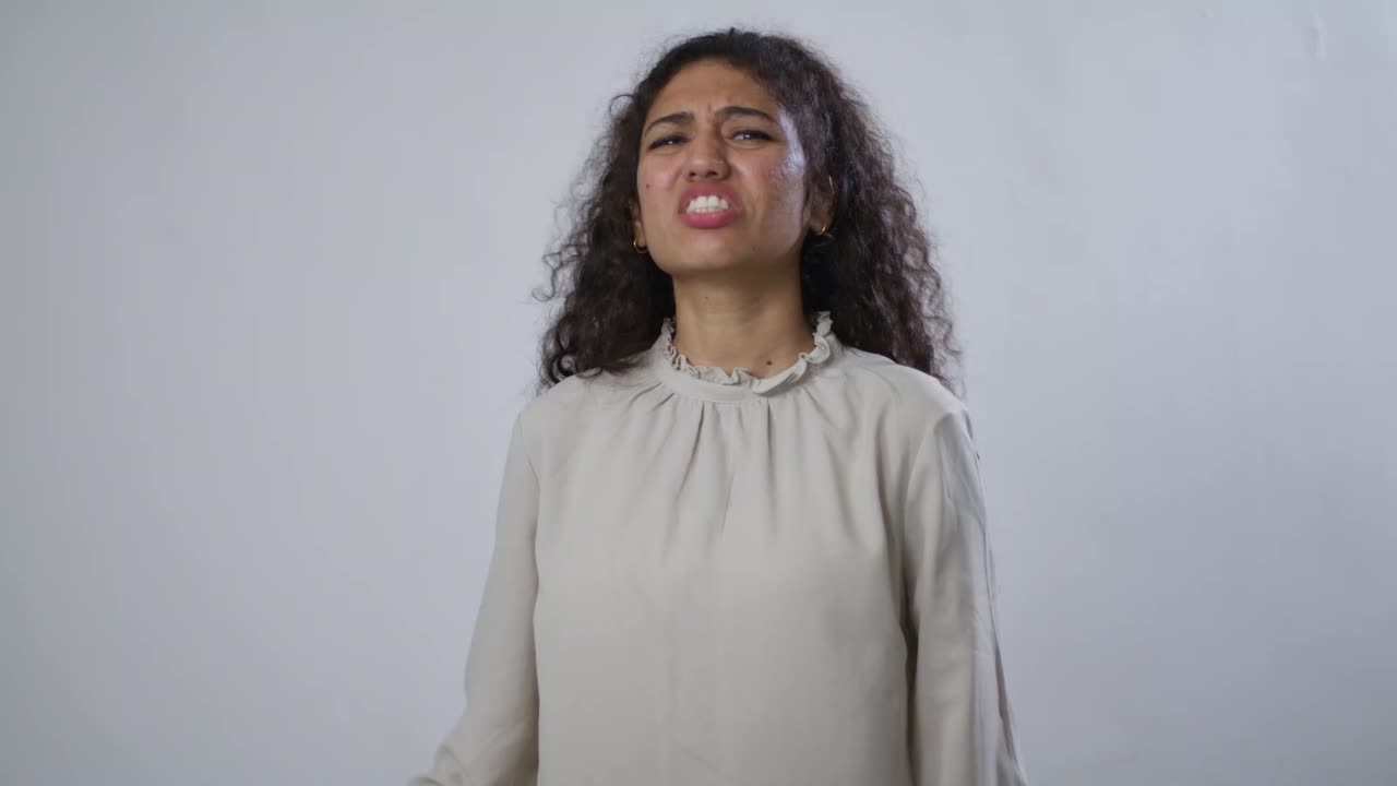 Una giovane donna sud asiatica con capelli castani ricci stringe i denti e sembra arrabbiata o frustrata