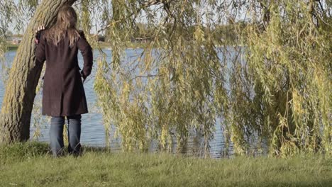 woman standing beside weeping willow tree at water side