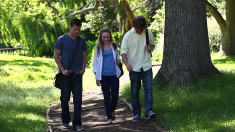 three students talking to each other as they walk on a park trail