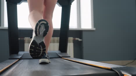 back view of woman walking on treadmill inside gym facility with visible treadmill power cable plugged into outlet on wall near window under soft natural light