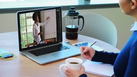 Kaukasische-Lehrerin-Trinkt-Kaffee-Und-Macht-Sich-Notizen,-Während-Sie-Einen-Videoanruf-Auf-Dem-Laptop-Führt