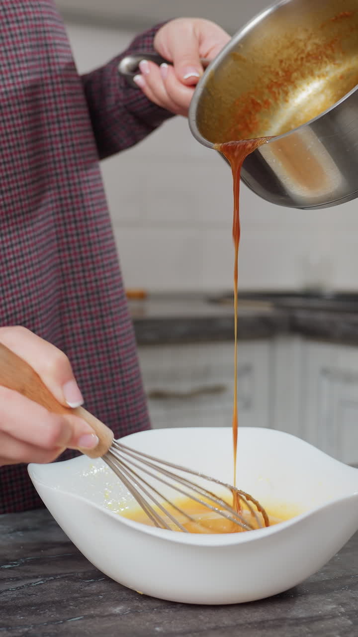 vista parcial de una persona moviendo una mezcla de huevos en un cuenco blanco mientras vierte sopa caliente y sabrosa de la olla, las manos golpeando activamente y vertiendo en una cocina moderna con encimera de mármol oscuro