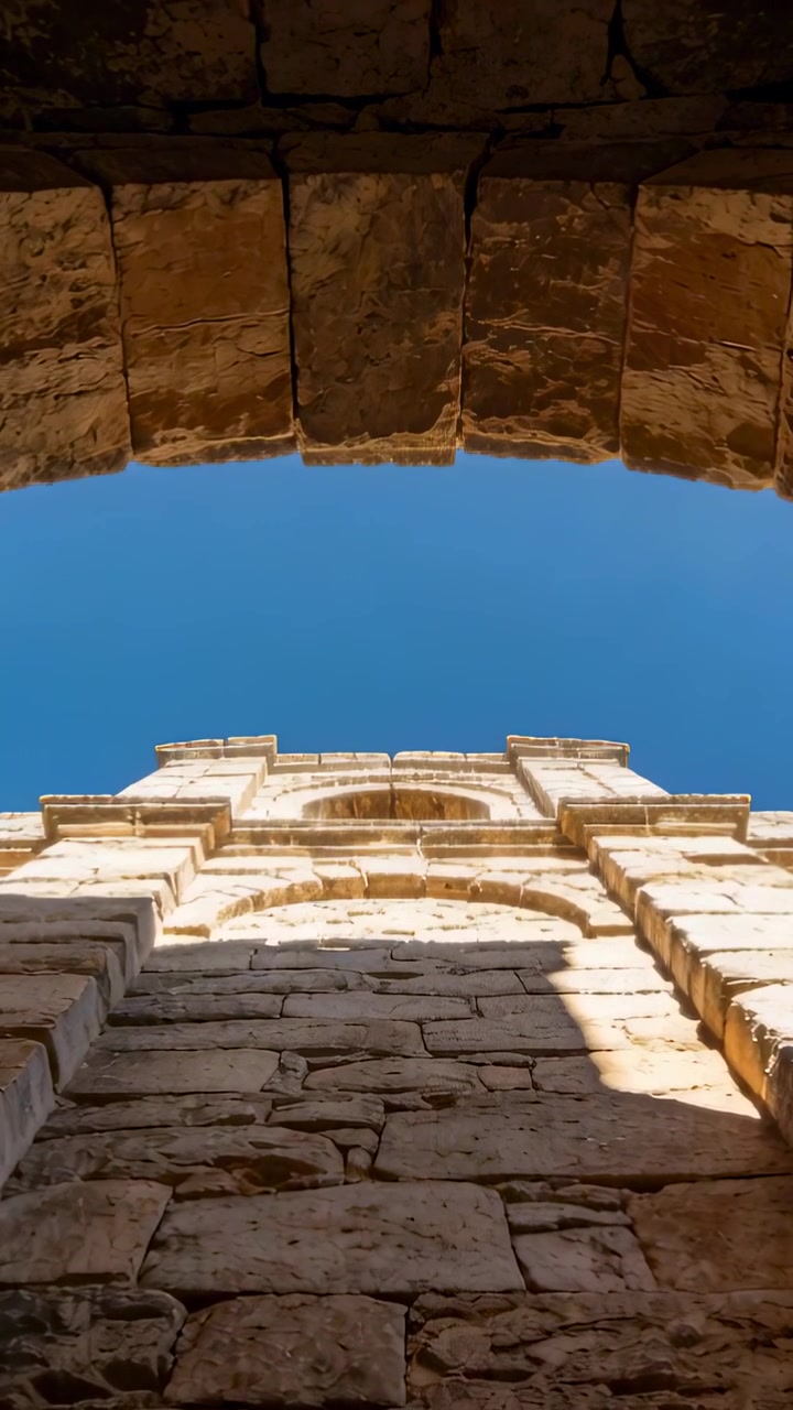 Video verticale: Telecamera che si inclina mostrando un arco in pietra e una facciata all'ingresso, rivelando il cielo e l'ombra dell'arco.