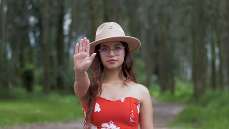 Young-woman-in-a-red-summer-dress-and-hat-raises-her-hand-as-a-stop-sign