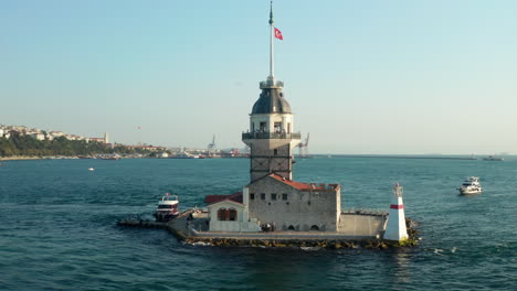 Rodeando-La-Torre-De-La-Doncella-Con-La-Bandera-De-Turquía-En-El-Río-Bósforo-Oceánico-En-Estambul-En-La-Hermosa-Luz-De-La-Tarde,-Toma-Aérea-De-Establecimiento