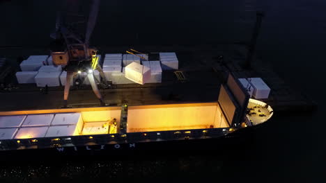 Crane loading the hull of a cargo ferry at nighttime - aerial orbit