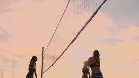 slow motion low angle close up sun flare: athletic girl playing beach volleyball jumps in the air and strikes the ball over the net on a beautiful summer evening. caucasian woman score a point.