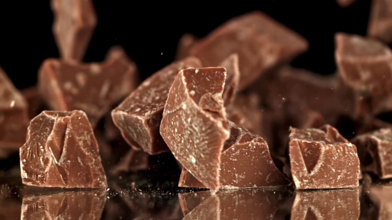 Pezzi di cioccolato che cadono e si disperdono su una superficie nera riflettente al rallentatore