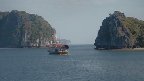 Parallax-drone-view-of-a-boat-sailing-in-the-bay-near-Cat-Ba-Island-and-turquoise-water,-Vietnam