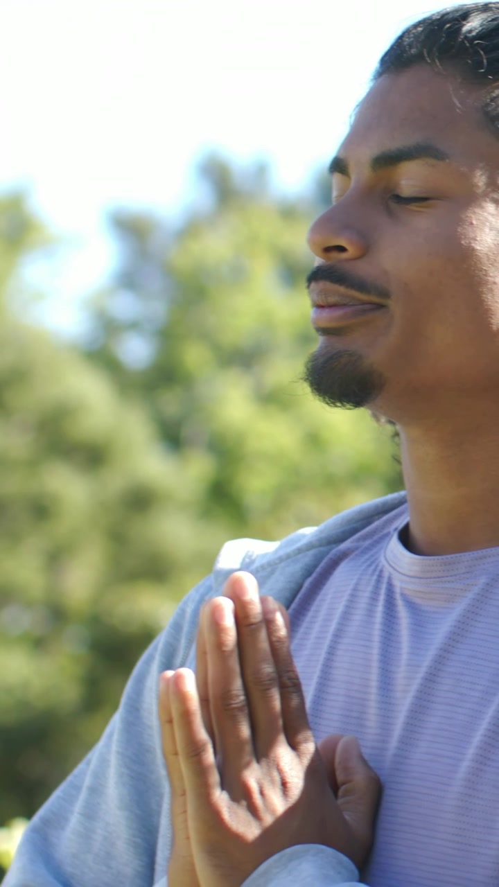 Vertical video: Camera pulling back man centering palms together in garden hoodie, copy space