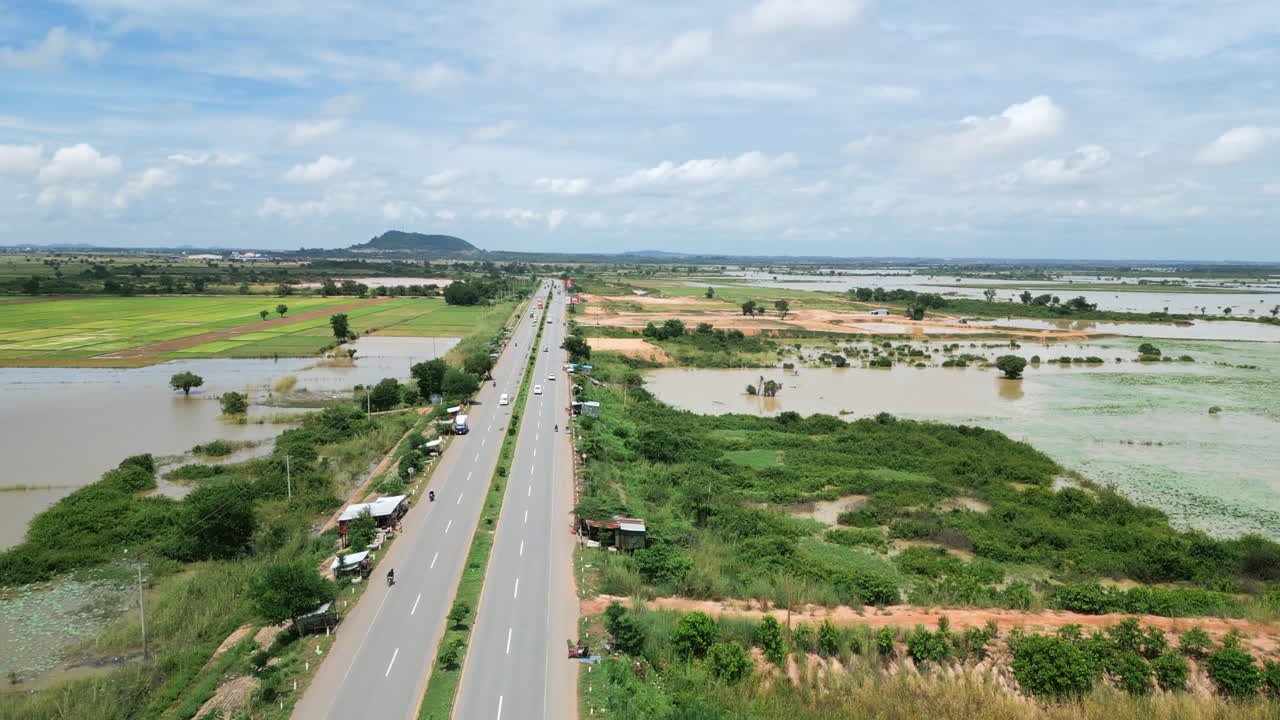 Aerial shot of highway cutting through flooded Cambodian farmland, with distant hills in the background