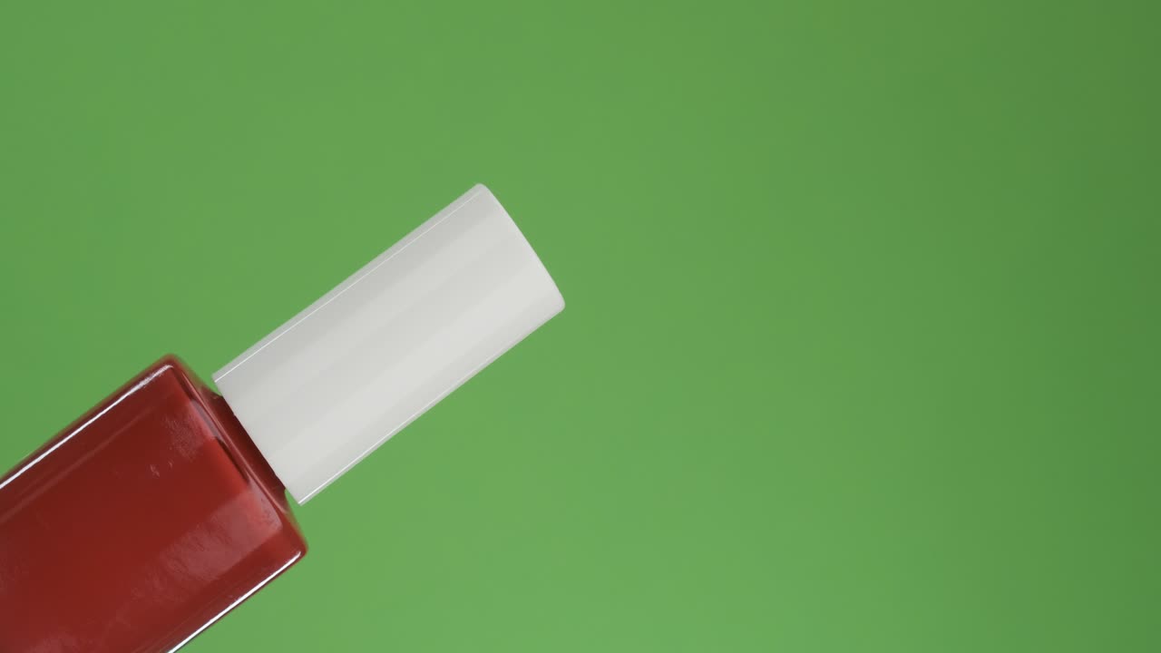 Rotazione diagonale di una bottiglia di smalto per unghie in vetro. Isolato su verde.