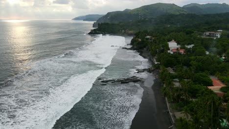 Vista-Aérea-Que-Avanza,-Vista-Panorámica-De-La-Luz-Del-Sol-Que-Se-Refleja-En-La-Playa-En-Bitcoin-Beach-En-El-Salvador,-México,-Montaña-Y-Cielo-Azul-En-El-Fondo