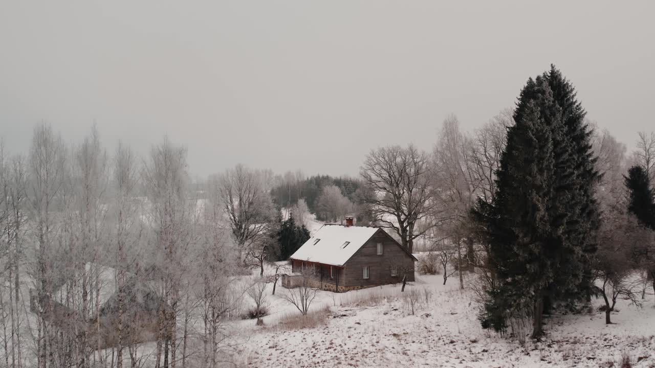 Family home in the countryside on a white winter day with lots of snow and frost on the trees. Aerial drone shot in the suburbs on a cloudy day.