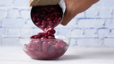 pouring canned kidney beans into a glass bowl