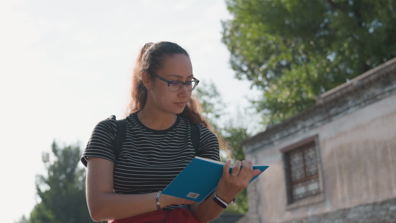 Individuo che scrive in un contesto storico all'aperto. Studente intento a scrivere con zaino in spalla, sotto la luce del sole. Giovane studioso che prende appunti davanti a un'antica struttura in pietra in una giornata di sole.