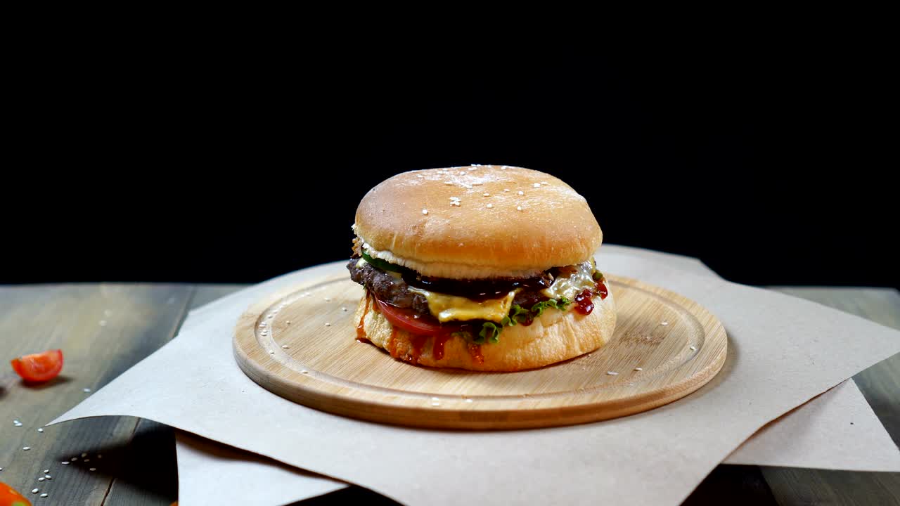 Fresh appetizing hamburger rotating on black background. Seamless loopable shot
