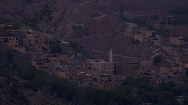 Ripresa cinematografica con teleobiettivo di un remoto villaggio berbero incastonato sui pendii rocciosi dell'Atlante in Marocco, che mette in risalto le tradizionali case in adobe, i sentieri tortuosi e un minareto in primo piano al crepuscolo