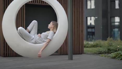 young woman in white futuristic swing in the yard outdoors