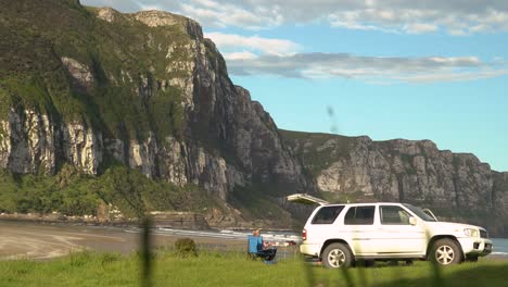 Female-camping-and-relaxing-in-front-of-beach-view-cliffs-next-to-her-four-wheel-drive-car
