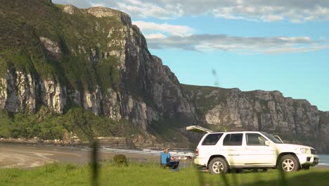 mujeres acampando y relajándose frente a los acantilados con vista a la playa junto a su auto con tracción en las cuatro ruedas