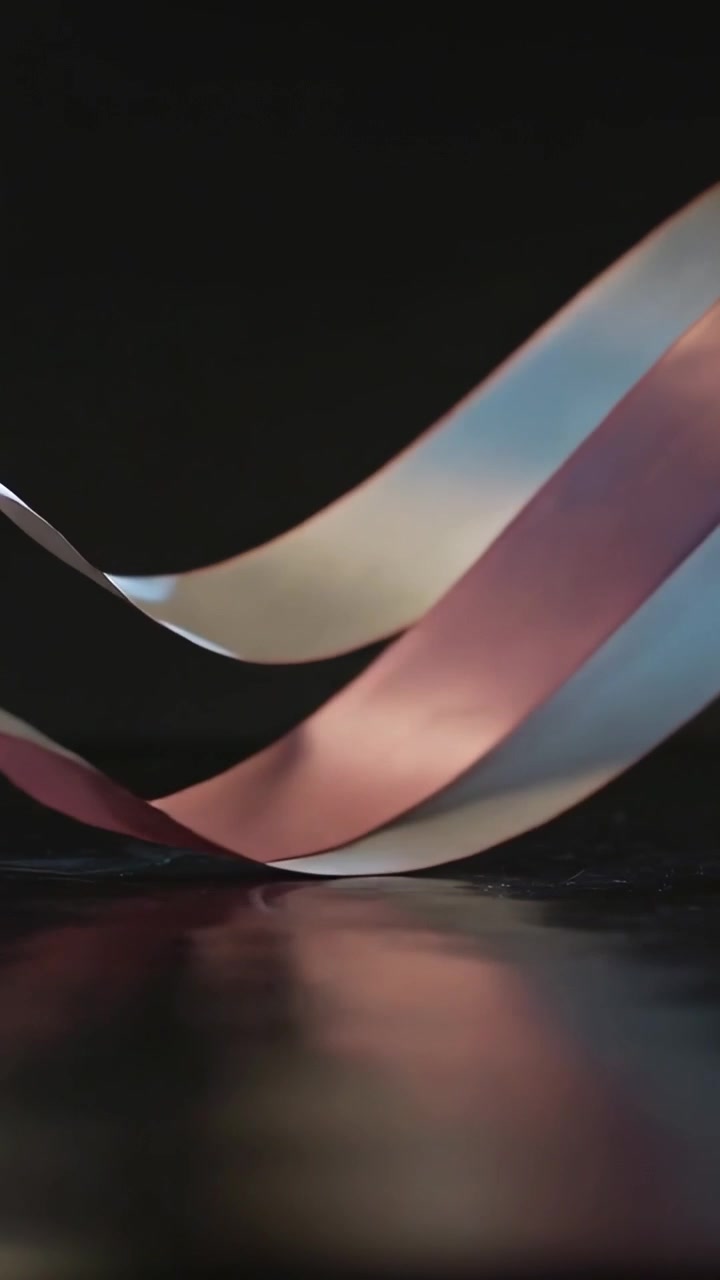 Vertical video: Swaying three satin ribbons falling crossing settling on tabletop with studio light