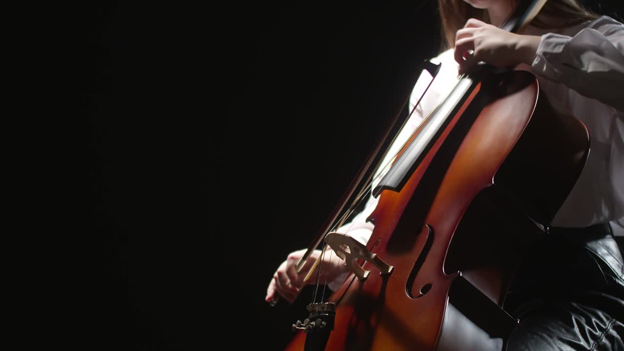 Girl's hand playing cello, closeup on black background. Cello strings and bow closeup, side view. Studio shooting