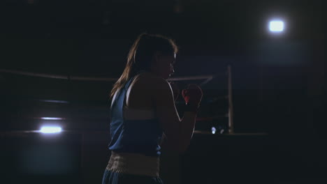 professional beautiful female boxer otbryvatyvat blows conducting a fight with a shadow in a dark hall of the hall in slow motion in blue clothes and red bandages on her wrists. flying around the object. steadicam shot