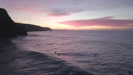 surfistas al atardecer y acantilados de silueta en cornwall