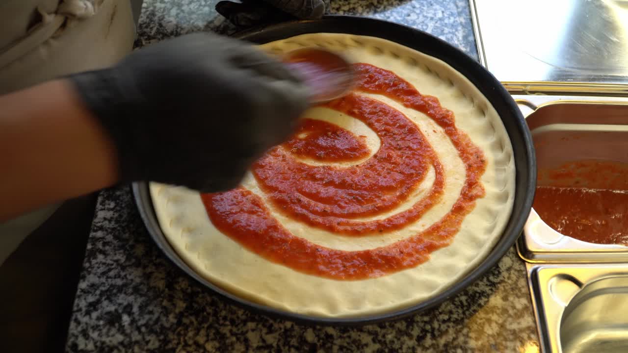 añadiendo salsa de tomate a la masa de la pizza