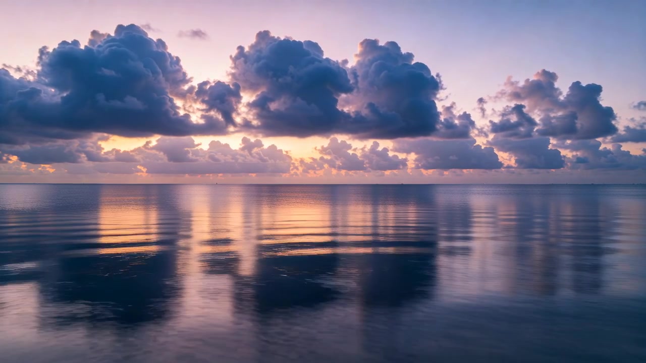 Shifting cumulus bank and reflection moving over calm sea, sunlight warming horizon and rippling