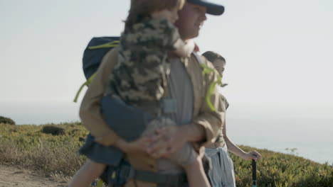 father and children hiking together, walking along path, approaching camera