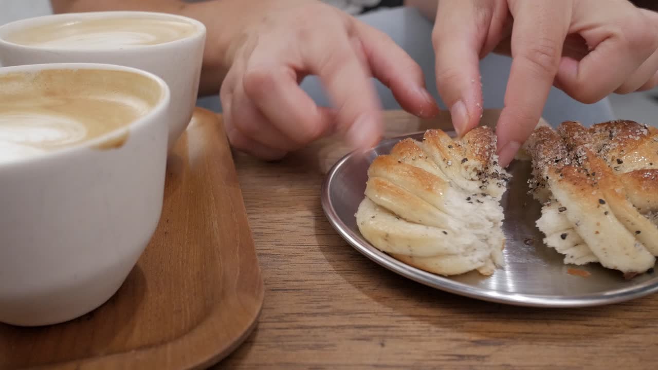 Delicious cardamom buns served with coffee, hands reaching to break apart the sweet pastry