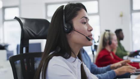 Frau-Trägt-Headset-Und-Spricht,-Während-Sie-Auf-Ihrem-Schreibtisch-Im-Büro-Sitzt