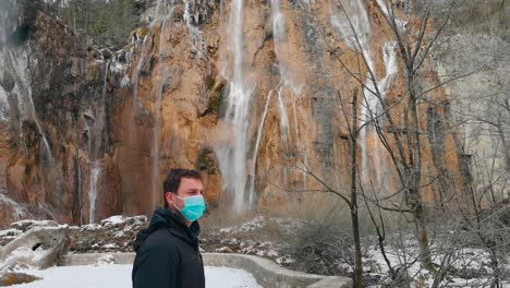 En-Un-Parque-Nacional-Croata,-Un-Hombre-Con-Una-Máscara-De-Operación-Simboliza-Las-Precauciones-Contra-Una-Pandemia-En-Medio-De-Una-Belleza-Escénica-Con-Agua-Moviéndose-Al-Fondo