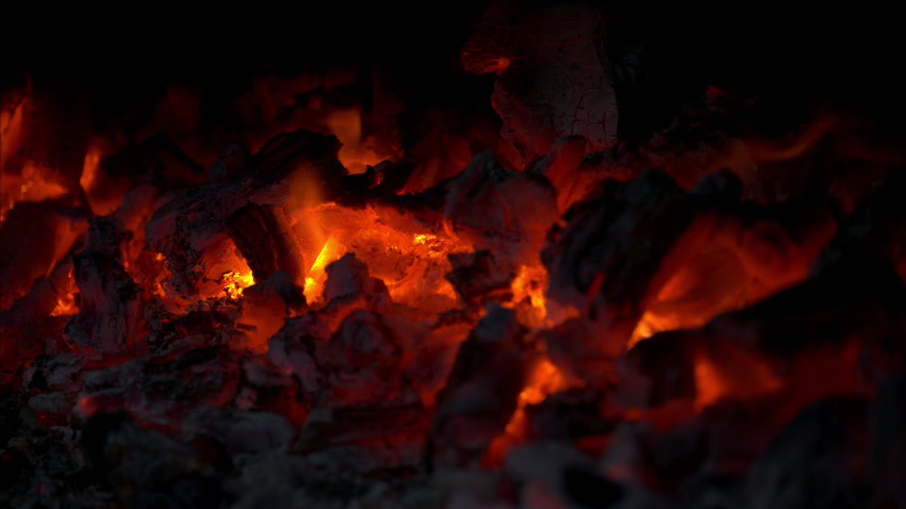 Slow motion close up of a pile of burning red hot charcoal with flames coming out