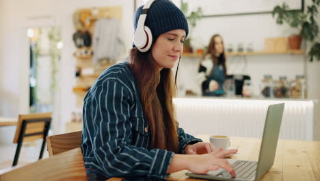 Woman working on a laptop in a cafe with headphones