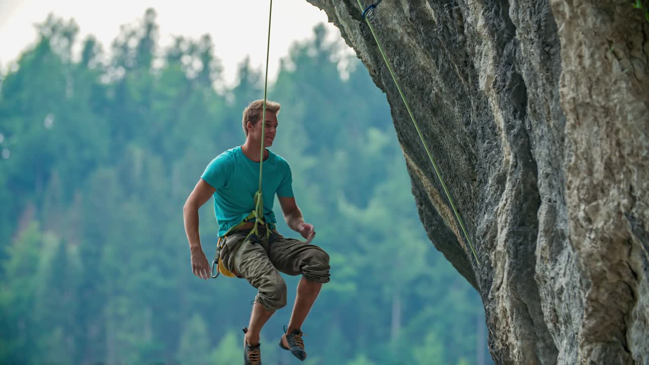 un hombre escalando un risco vertical intenta agarrarse a una presa, pero falla y se cae