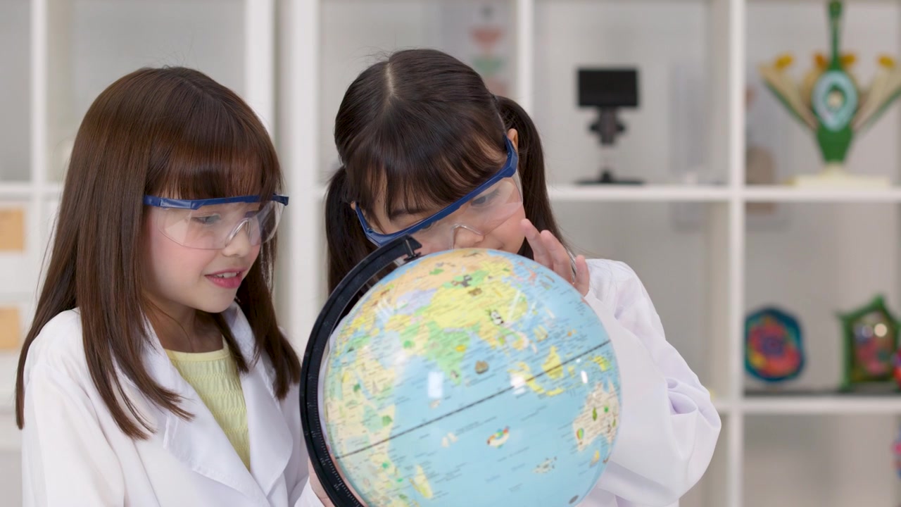 Estudiantes de primaria con gafas de seguridad y batas de laboratorio estudian un globo terráqueo en un aula de ciencias
