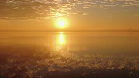 Der-Reiher-Steht-An-Den-Felsen,-Während-Sich-Der-Sonnenuntergang-Zur-Goldenen-Stunde-Im-Welligen-Wasser-Spiegelt