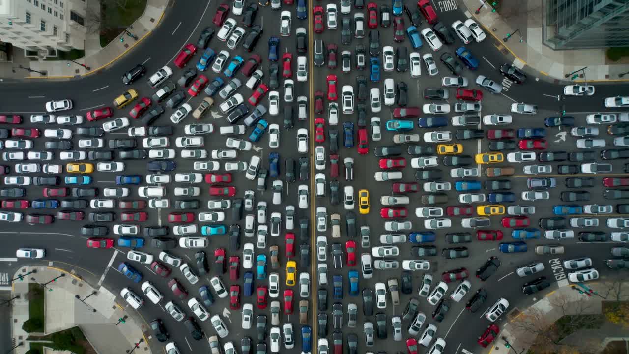 Heure de pointe : voitures et taxis avançant lentement dans une intersection à plusieurs voies du centre-ville, avec terre-plein central.