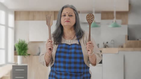 Confident-Indian-aged-housewife-posing-with-spoon-and-spatula